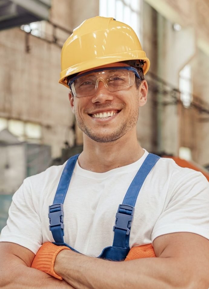 cheerful male builder in safety helmet standing at construction site e1638240620268